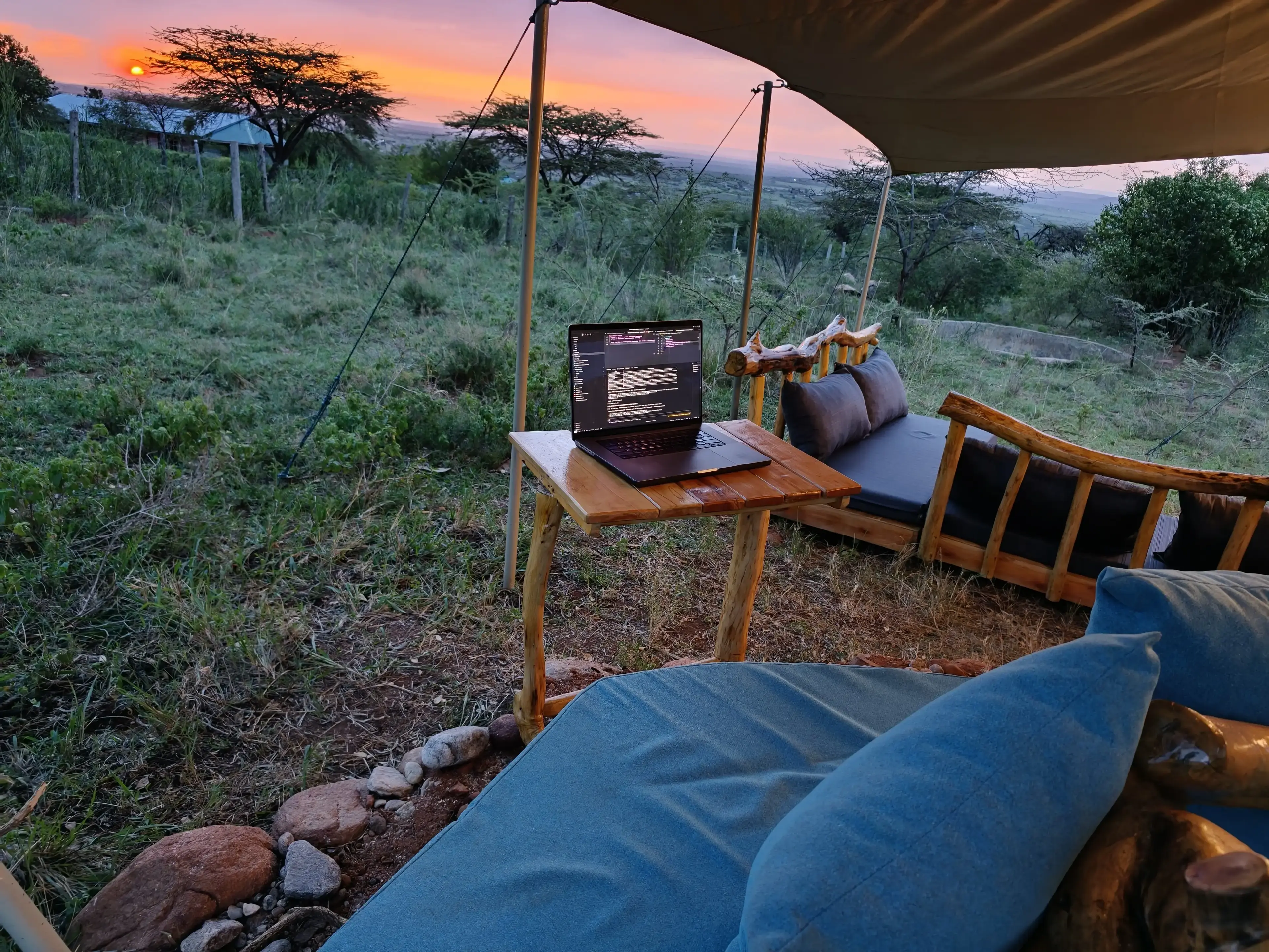 A laptop on a table under the canopy, with floor cushions