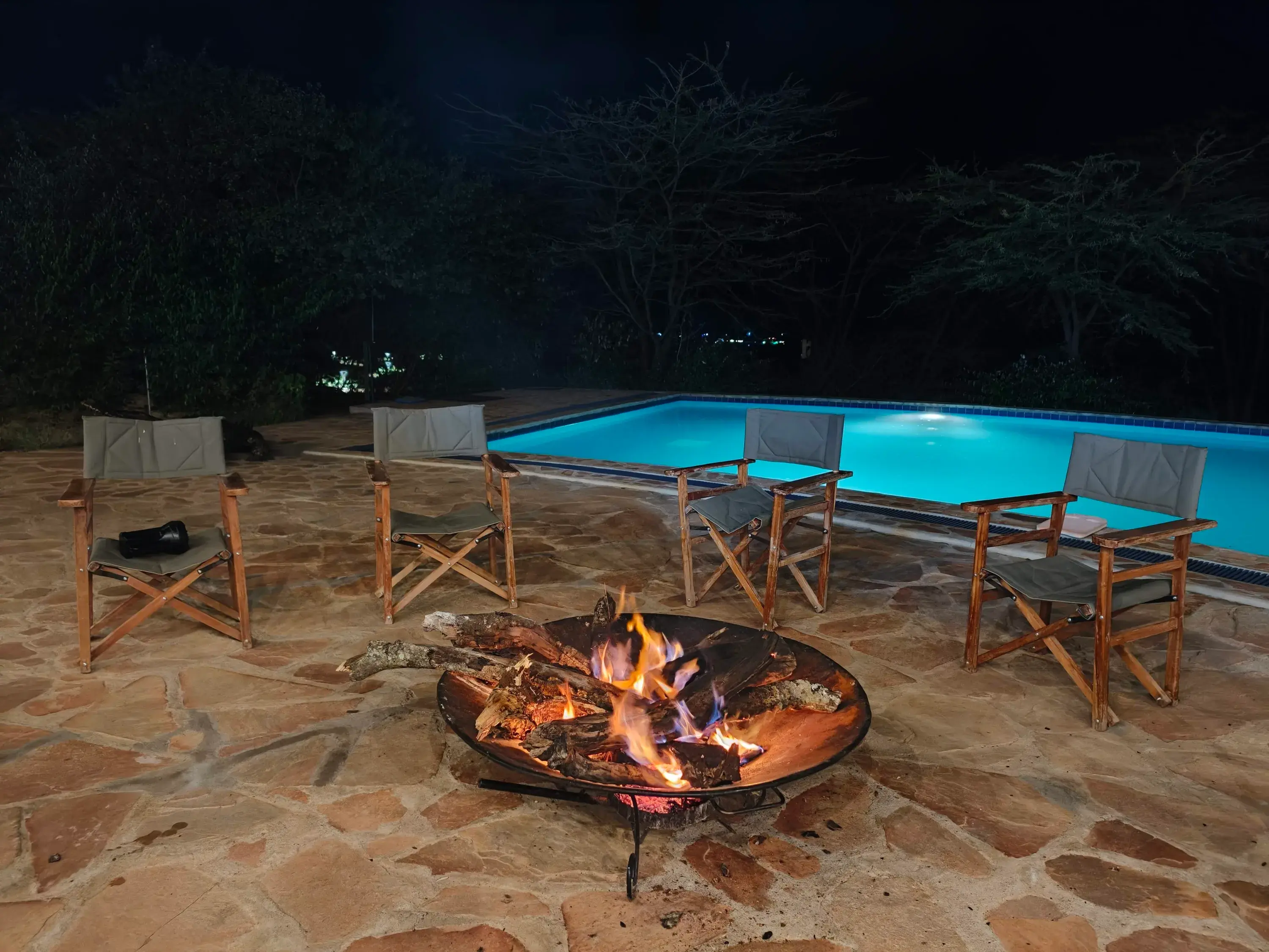 Fire pit and safari chairs beside the lit pool at night