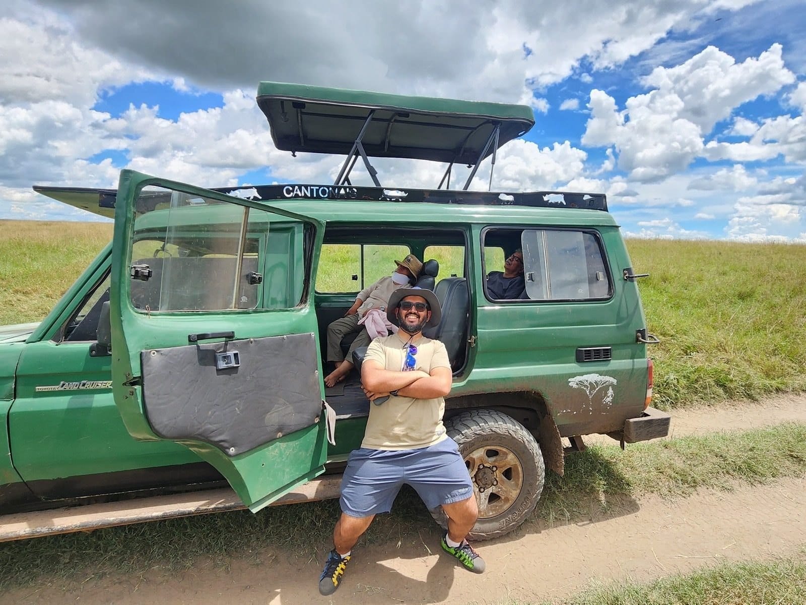 Nikhil sitting on the step of an open safari Land Cruiser on a game drive in the Maasai Mara.